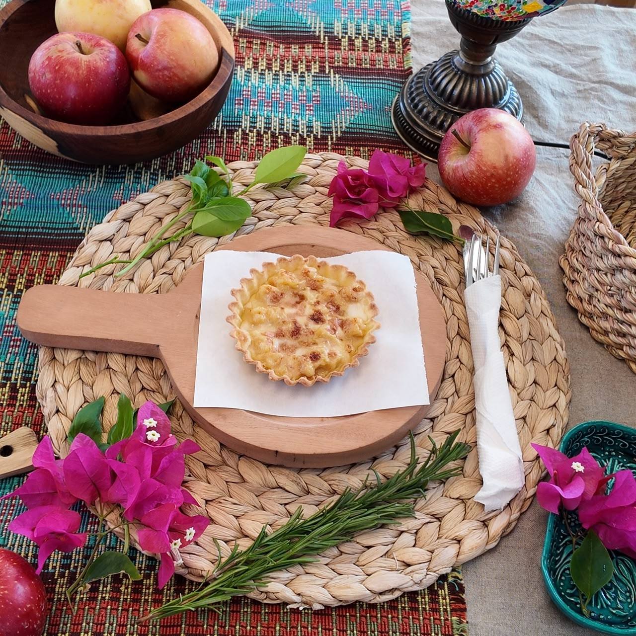 A golden quiche on a wooden board, with bougainvillea and rosemary