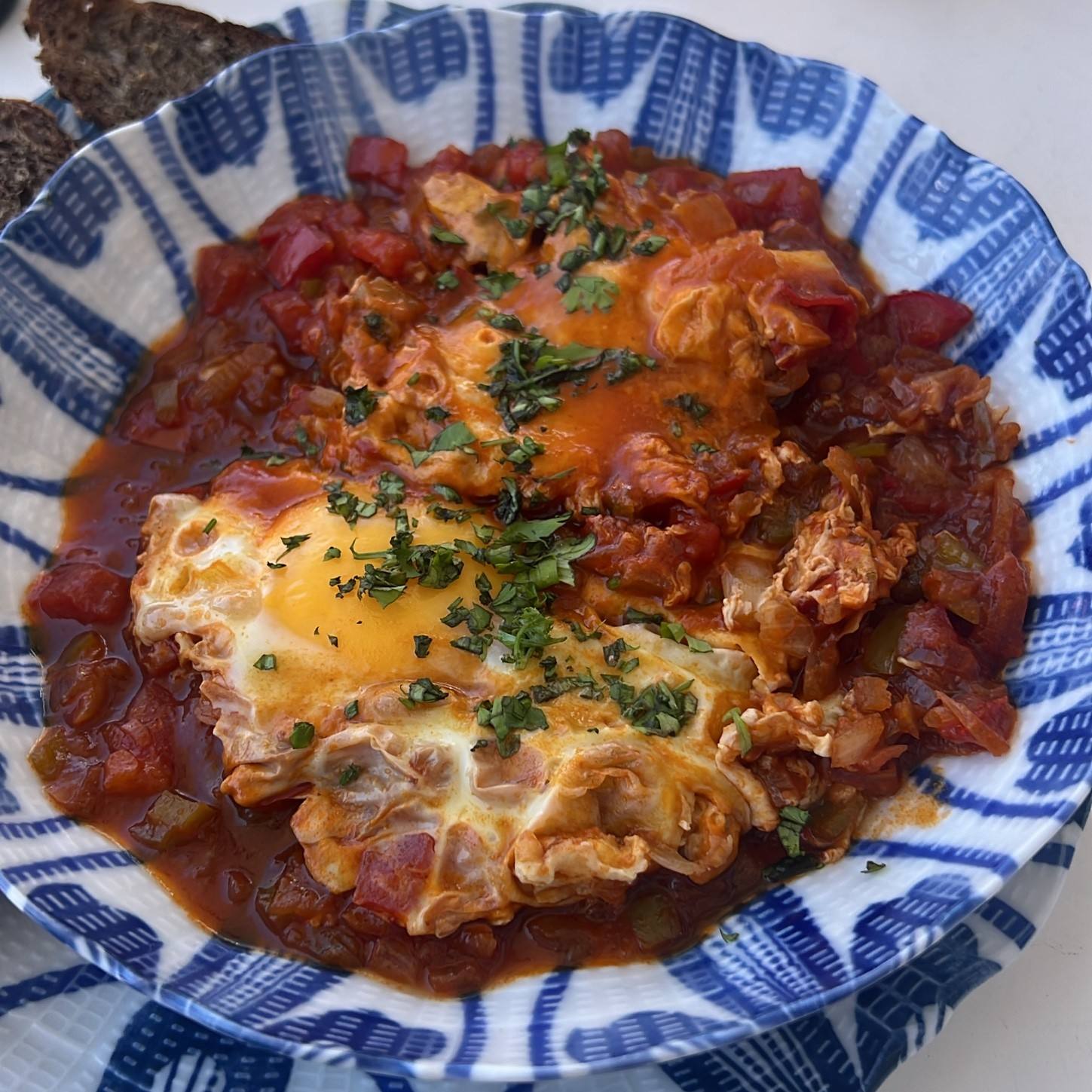 Shakshuka with two eggs and parsley in a blue and white Tunisian bowl